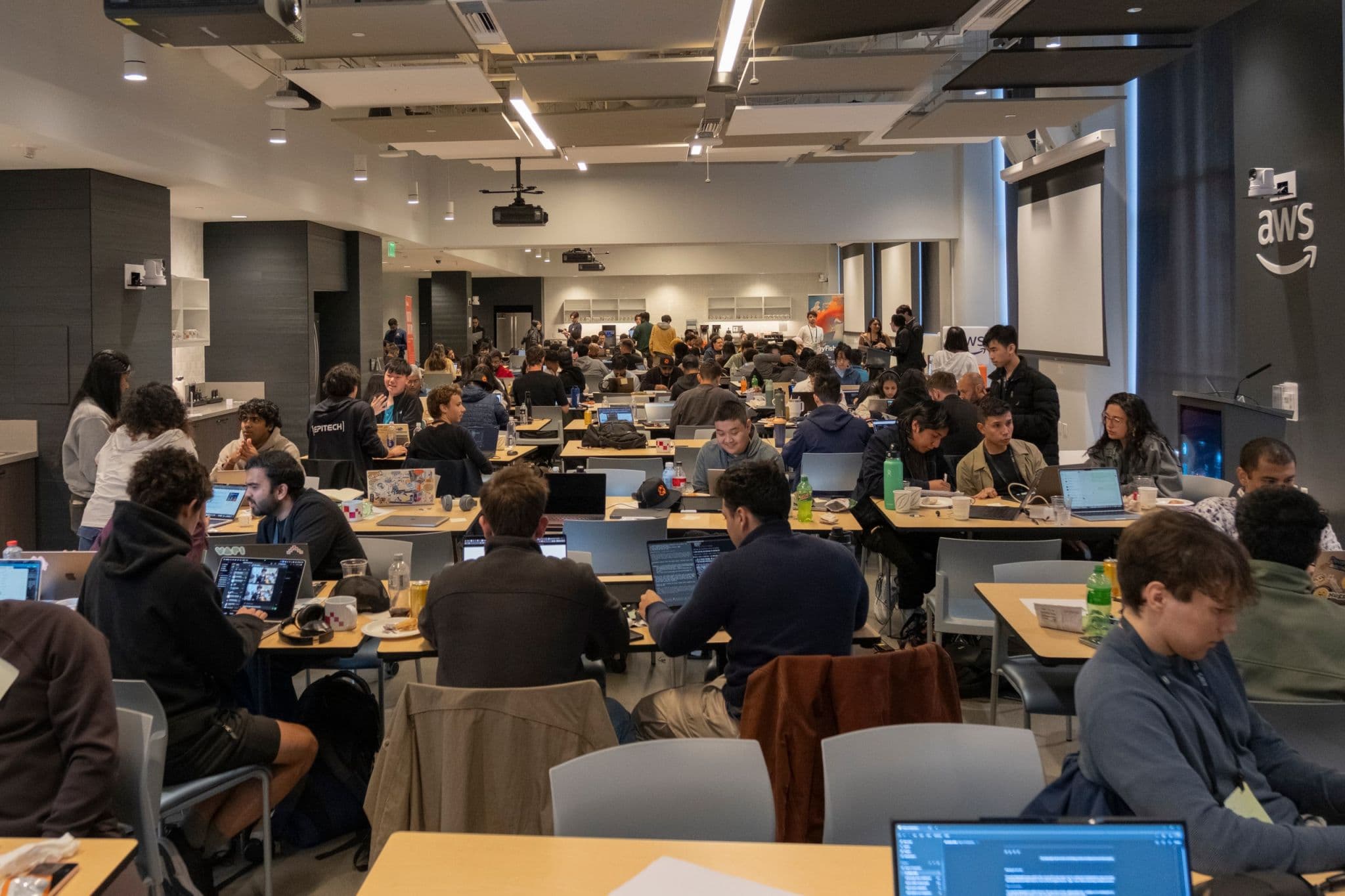 Developers working on laptops during a tokens& hackathon at an AWS venue.